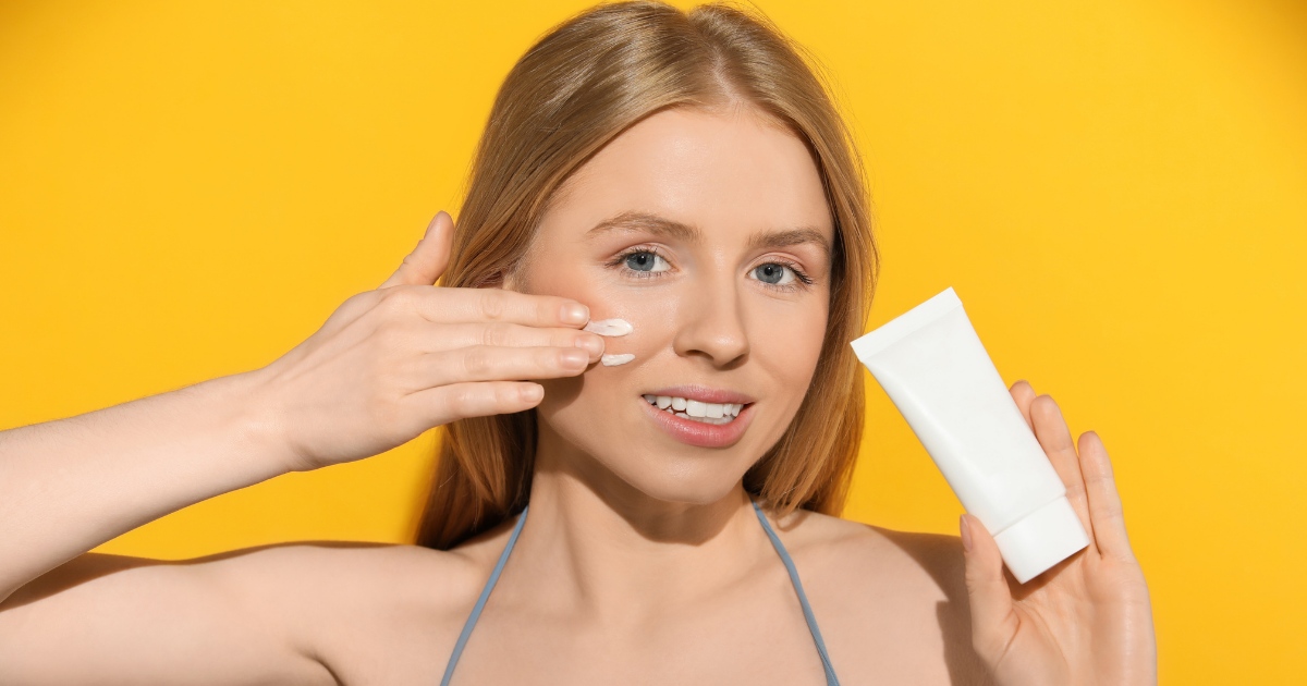 woman applying sunscreen to her face in a sunlit bathroom, representing healthy post-treatment habits