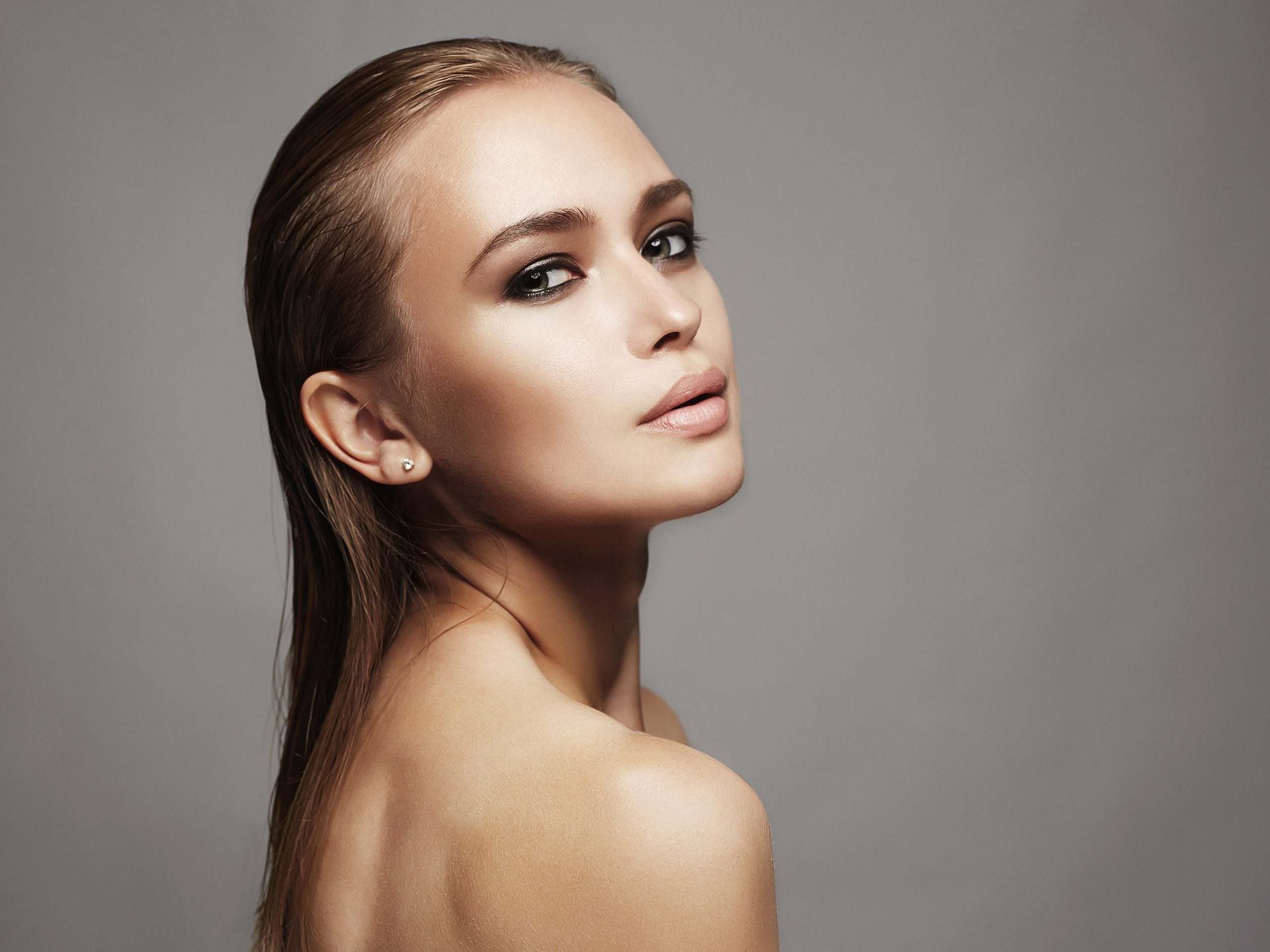 Woman with blonde sleeked back hair looking over her shoulder with a sultry look.
